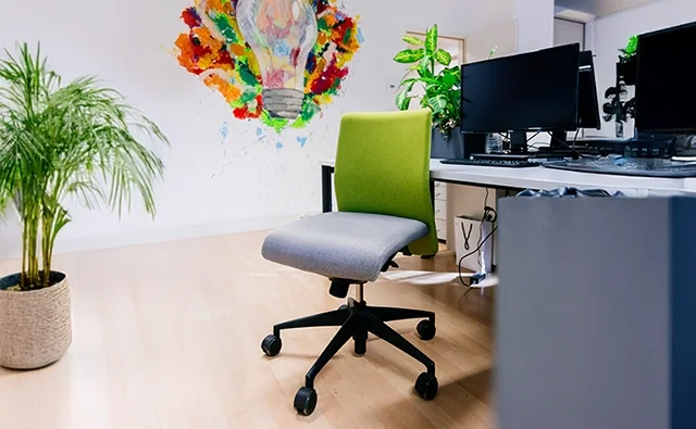 Leerer Bürosessel mit grünem Bezug vor einem Arbeitsplatz mit mehreren Computerbildschirmen im marketmind Büro.