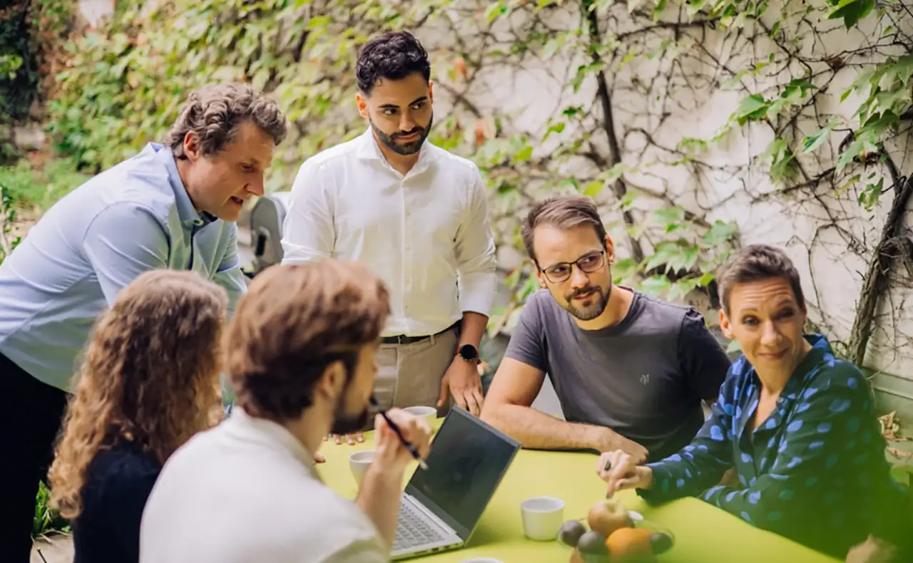 Gereon Friederes, Philipp Zelenka, Daniel Winzer, Dagmar Jiresch, Youssef Kawmi sitzen an einem Tisch im Garten des marketmind Büros zusammen mit Kunden und diskutieren angeregt. Auf dem Tisch stehen ein Laptop, Kaffeetassen und eine Schale mit Obst.
