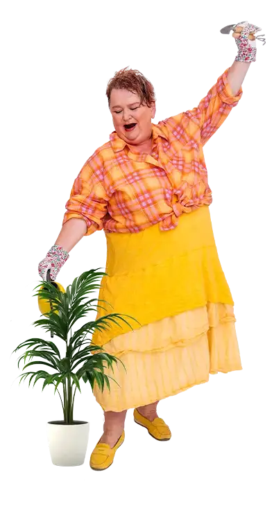 Lydia Croce tanzt fröhlich mit Gummihandschuhen, Giesskanne und bunter Kleidung um eine Topfpflanze herum - lebenslustig, farbenfroh und voller Humor.