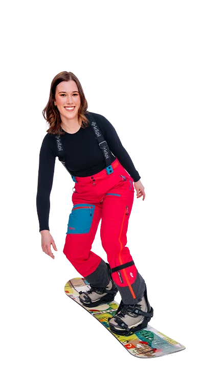 Lena Hammer, MA fährt in knallroter Skibekleidung auf einem Snowboard, lacht in die Kamera - voller Schwung und Spass im Schnee.