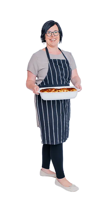 Anita Salamon trägt eine gestreifte Schürze und hält stolz ein frisch gebackenes Auflaufgericht in den Händen - herzlich, genussfreudig und mit Freude am Kochen.