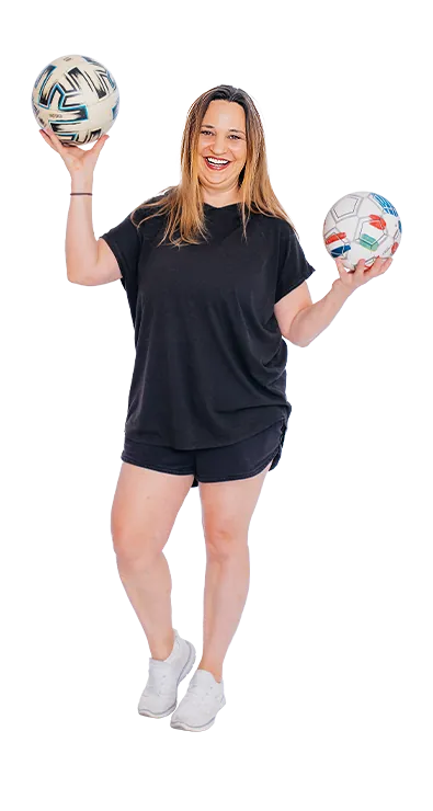Birgit Hütter steht lächelnd in Sportoutfit und hält zwei Fussbälle in den Händen - aktiv, spielerisch und voller guter Laune.