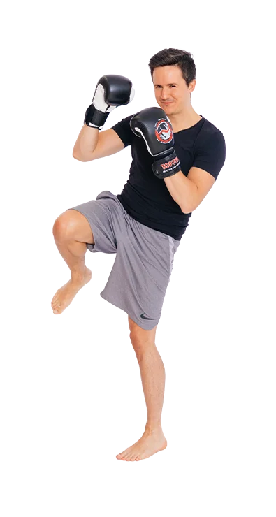 Daniel Mader steht in Kampfhaltung mit Boxhandschuhen und hebt das Knie - fokussiert, energiegeladen und sportlich.