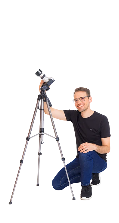 Daniel Winzer kniet lächelnd neben einem Stativ mit Kamera - mit Leidenschaft für Fotografie und den perfekten Moment.