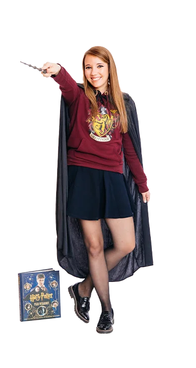 Jana Eisenbock steht in einem Harry-Potter-Kostüm mit Umhang und Zauberstab, ein Brettspiel auf dem Boden - fantasievoll, versunken in der Welt der Magie.