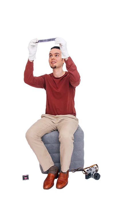 Jan-Bartl Koncel sitzt auf einem Hocker und trägt weisse Handschuhe, während er ein Fotonegativ prüfend gegen das Licht hält - mit Liebe zur analogen Fotografie.
