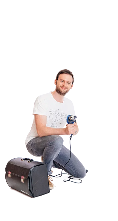 Lucas Pum hockt mit Bohrmaschine in der Hand neben einer Tasche, trägt Jeans und T-Shirt - technikbegeistert, kreativ und fokussiert.