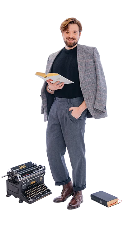 Philipp Zelenka steht elegant mit Buch in der Hand, neben sich eine alte Schreibmaschine und ein weiteres Buch - stilvoll, belesen und mit einem Hauch Retro-Charme.