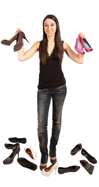 Raquel Herrero Pastor steht umgeben von einer Sammlung verschiedenster Schuhe und hält je ein Paar in jeder Hand - stilbewusst, entschlossen und voller Schuhleidenschaft.
