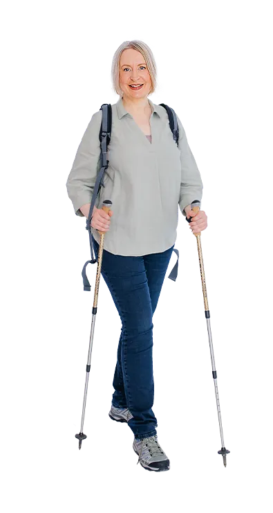 Sonja Ehrenberger geht mit Wanderstöcken und Rucksack lächelnd auf die Kamera zu - naturverbunden, aktiv und voller positiver Energie.