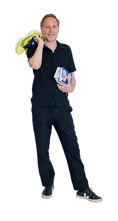 Dr. Thomas Winder trägt ein Paar Laufschuhe lässig über der Schulter und hält mehrere Bücher im Arm - sportlich, wissbegierig und stets in Bewegung.