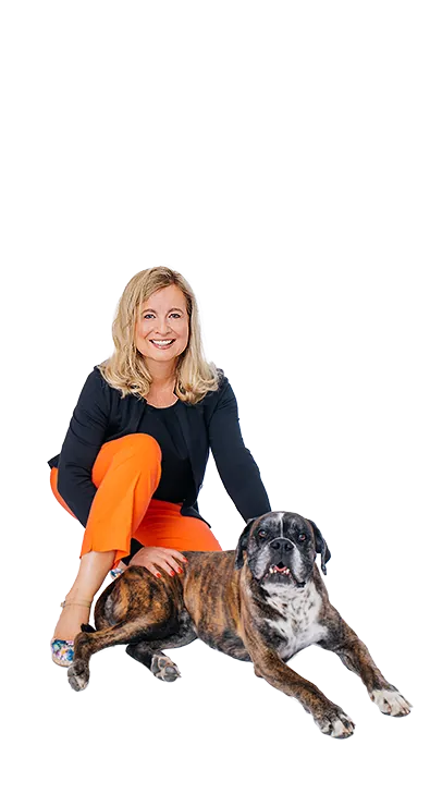 Dr. Verena Priemer kniet lächelnd neben einem braunen Hund, legt ihm die Hand auf den Rücken und strahlt Ruhe und Verbundenheit aus - tierlieb, herzlich und voller positiver Energie.